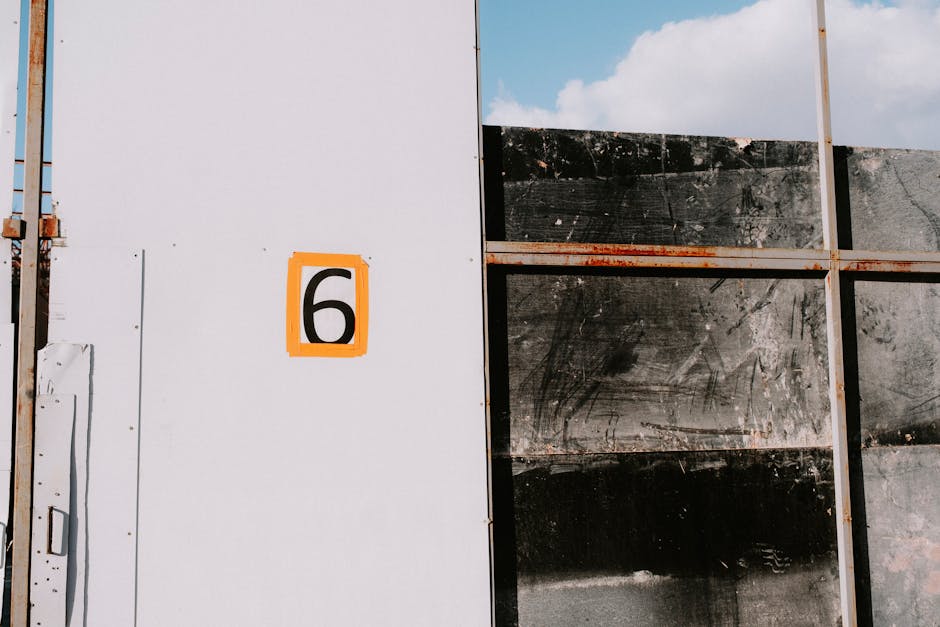 Close-up of a textured metal panel with a bold number six and rusty iron frame.