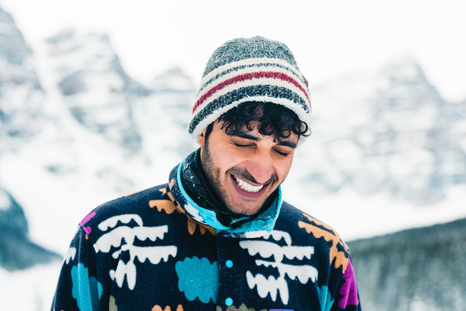 A cheerful man in colorful winter clothing, smiling against a snowy mountain backdrop in B