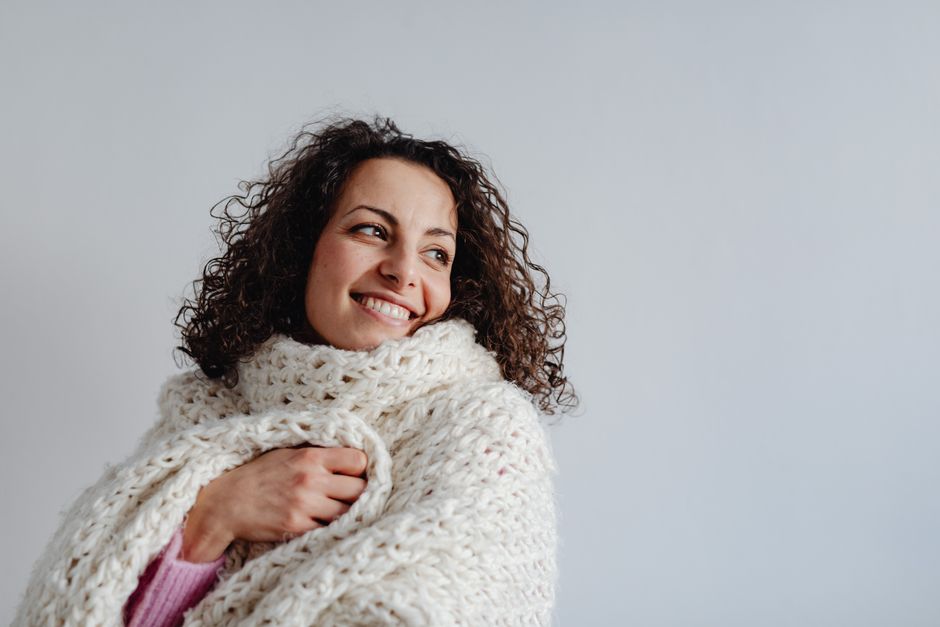 A cheerful woman with curly hair wrapped in a warm knit scarf, smiling in a cozy winter se