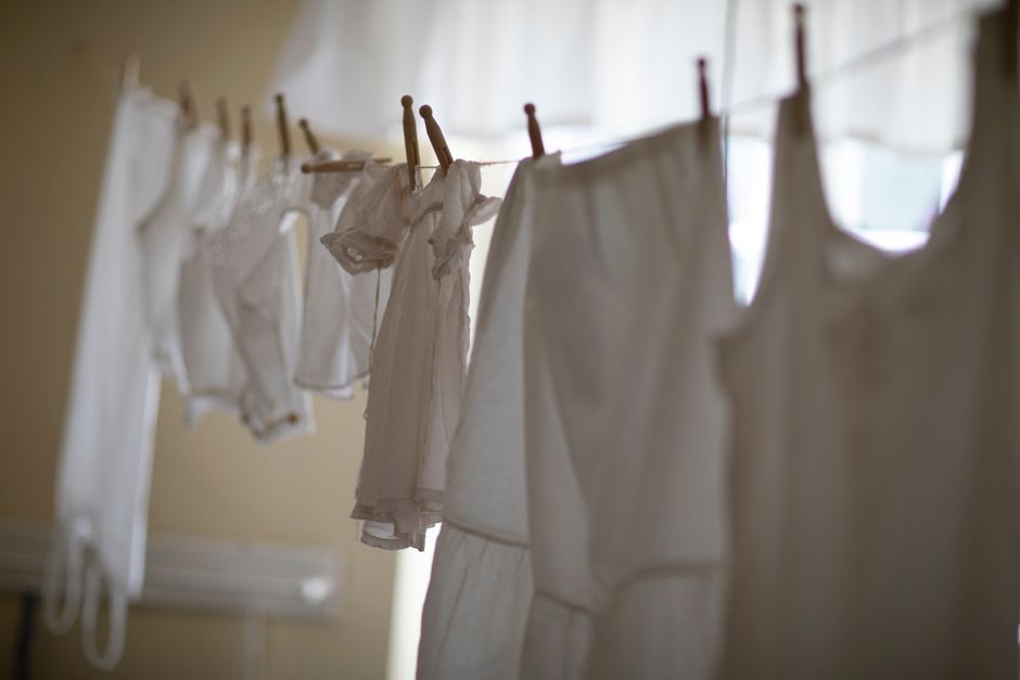 A row of white clothing hangs on a clothesline indoors, softly lit.