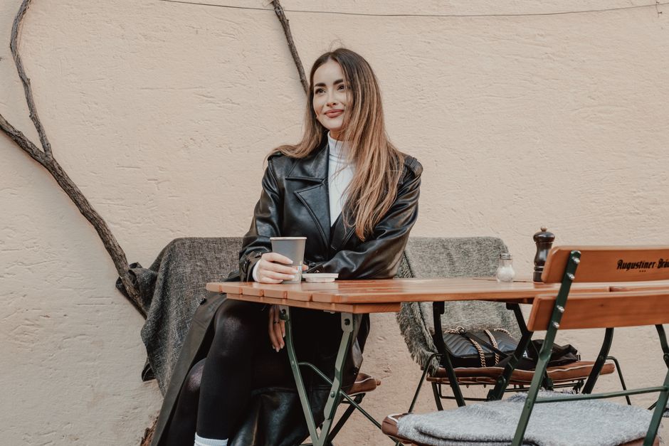 A stylish woman in a leather coat enjoying coffee at an outdoor cafe table, exuding elegan