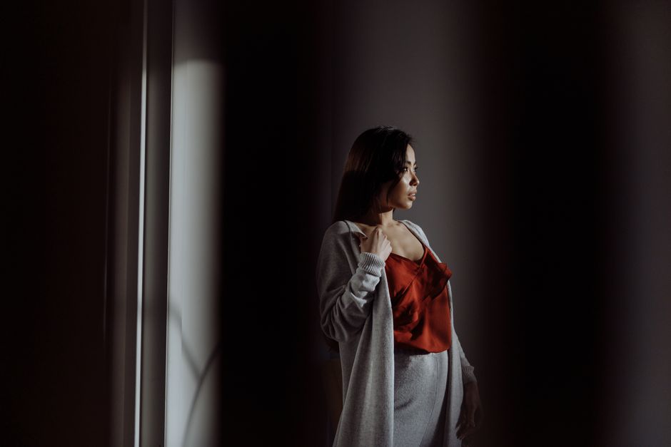 A thoughtful woman stands in soft light, wearing stylish loungewear.