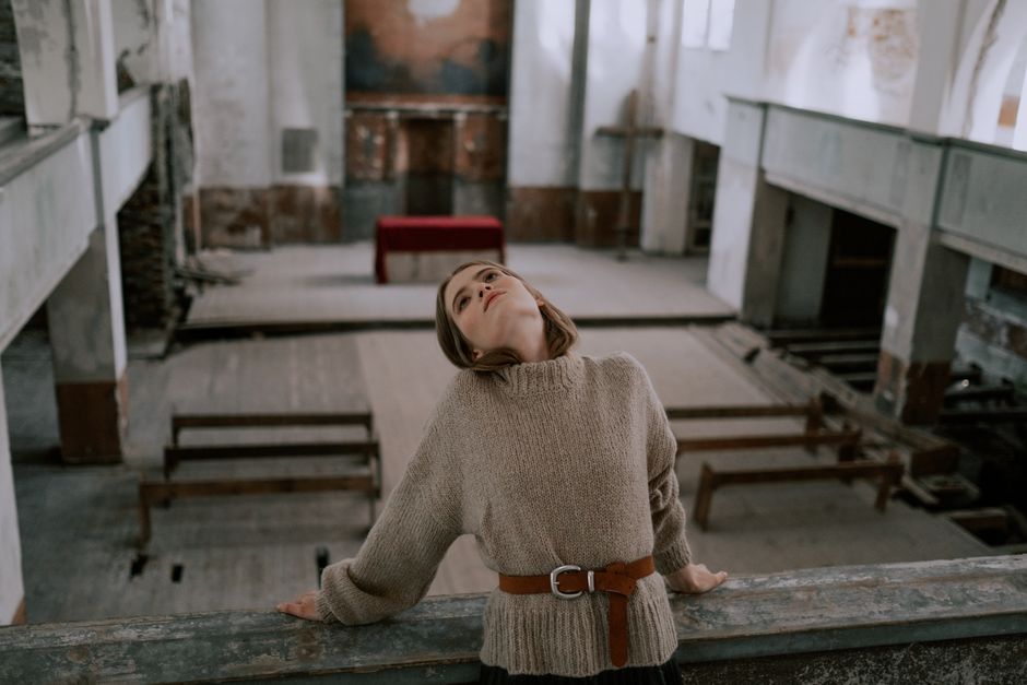 A woman leans back in a serene mood inside an abandoned church setting.