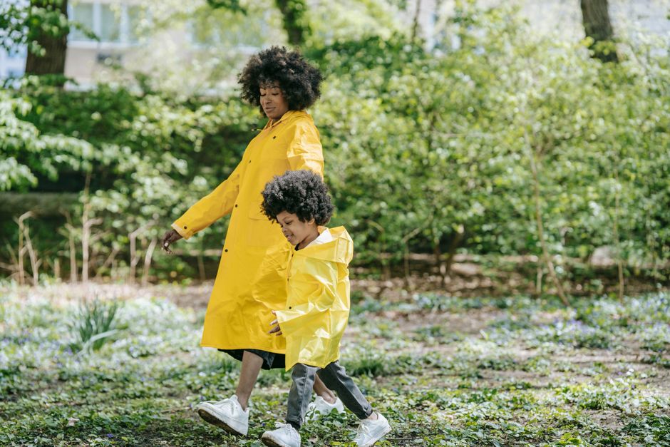 A joyful moment of a mother and child walking in matching yellow raincoats outdoors.