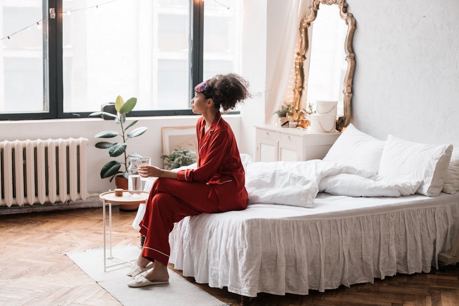 Woman in red pajamas sitting on bed with a glass of water, enjoying morning light.