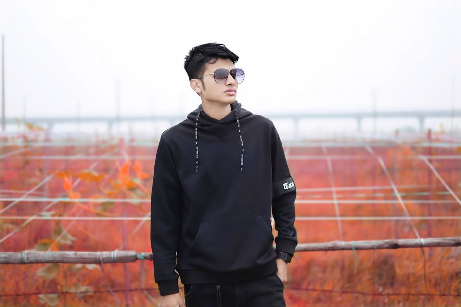 Young Asian male posing confidently in fall attire against autumn backdrop.