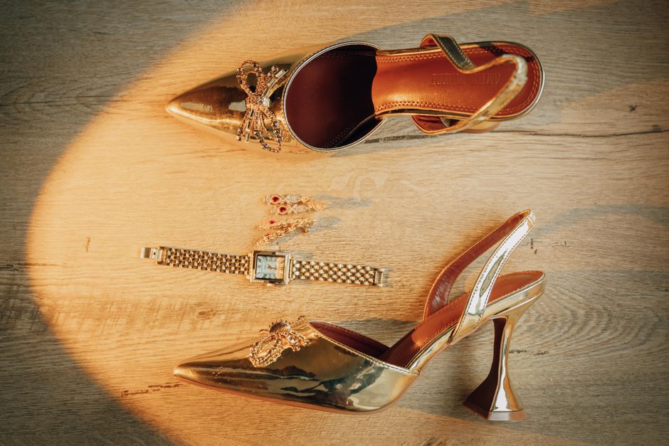 Stylish gold high heels paired with a watch and jewelry on a wooden floor, creating a luxurious fashion statement.