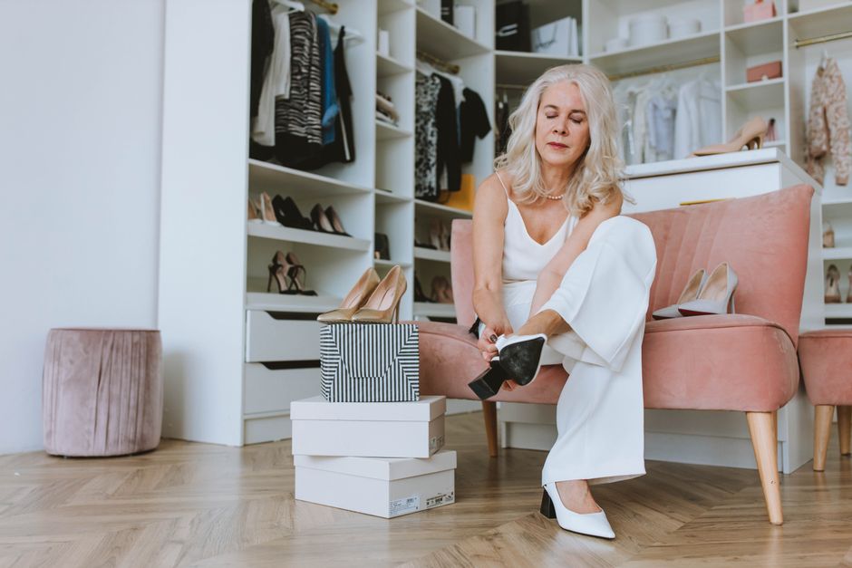 Elegant senior woman trying on shoes in a modern walk-in closet setting.