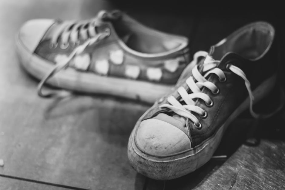 A pair of classic sneakers on a wooden floor in black and white photo.