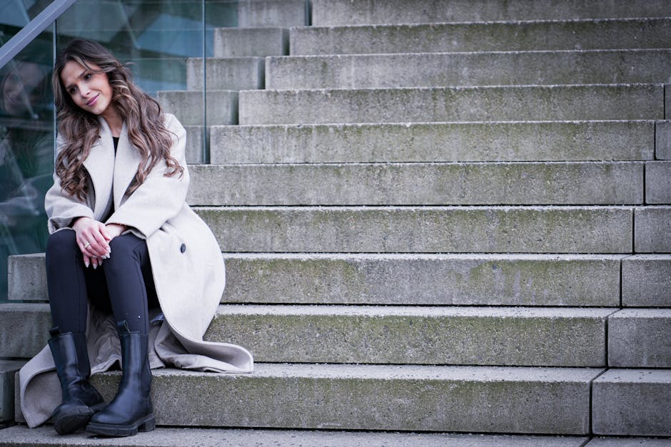Stylish woman with long hair sitting on stairs in Berlin, showcasing urban fashion.