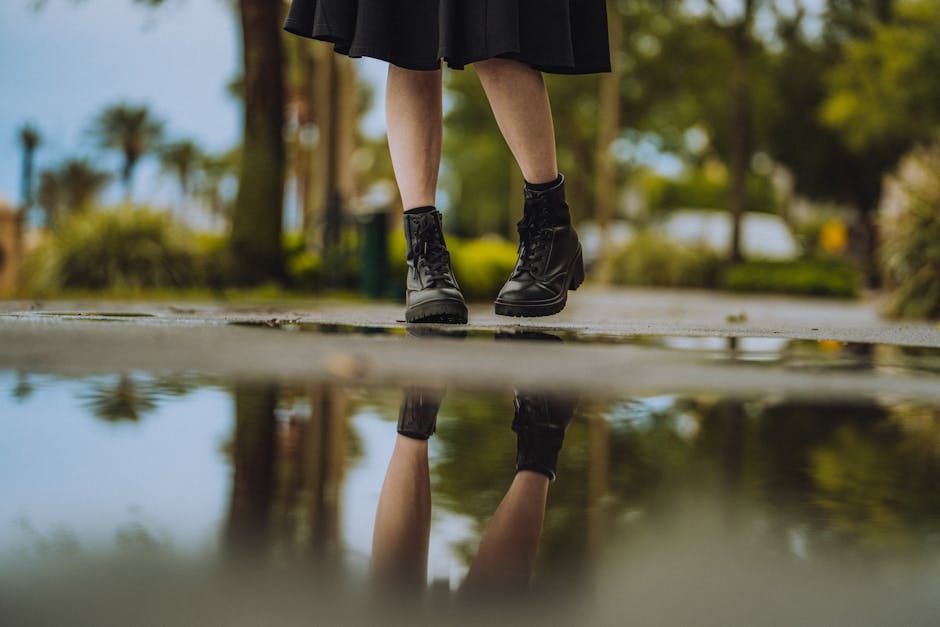Close-up of leather boots and their reflection in a puddle outdoors, showcasing fashion and nature.