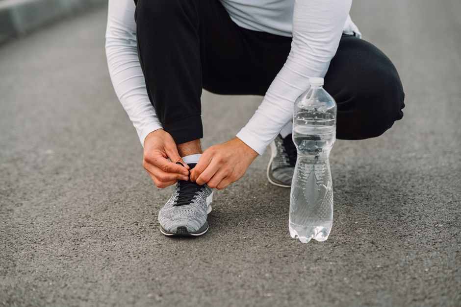 Runner tying shoelaces on the road with a water bottle beside. Fitness preparation.