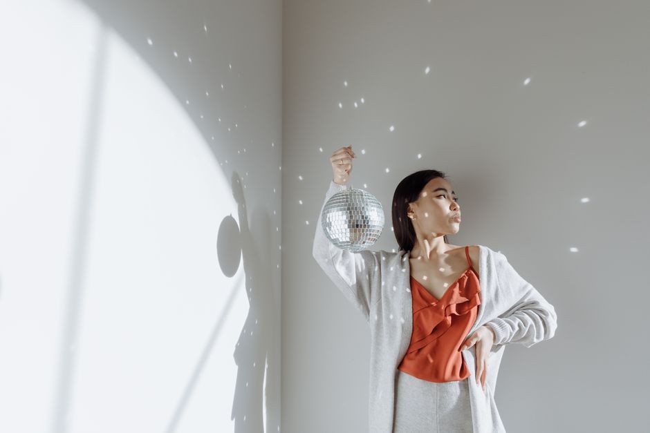 Fashionable woman posing with a disco ball, casting playful light reflections indoors.