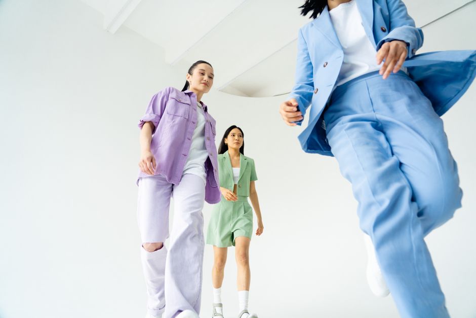 Dynamic low-angle shot of young women walking confidently in pastel suits, set against a b