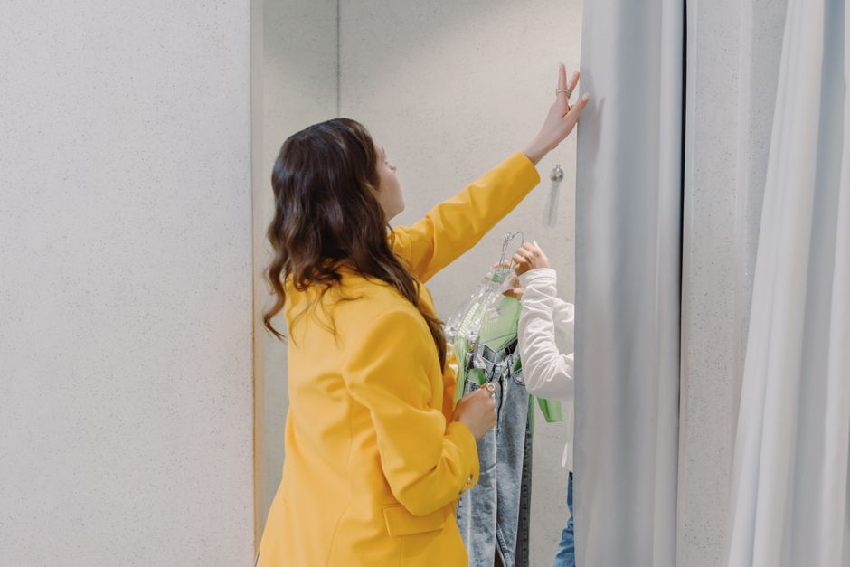 A woman helps select clothes in a modern fitting room, adding a personal touch to fashion shopping.