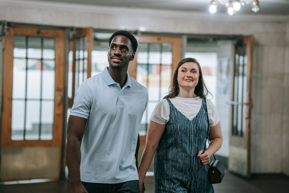 A joyful multiracial couple holding hands and walking indoors, exuding happiness.