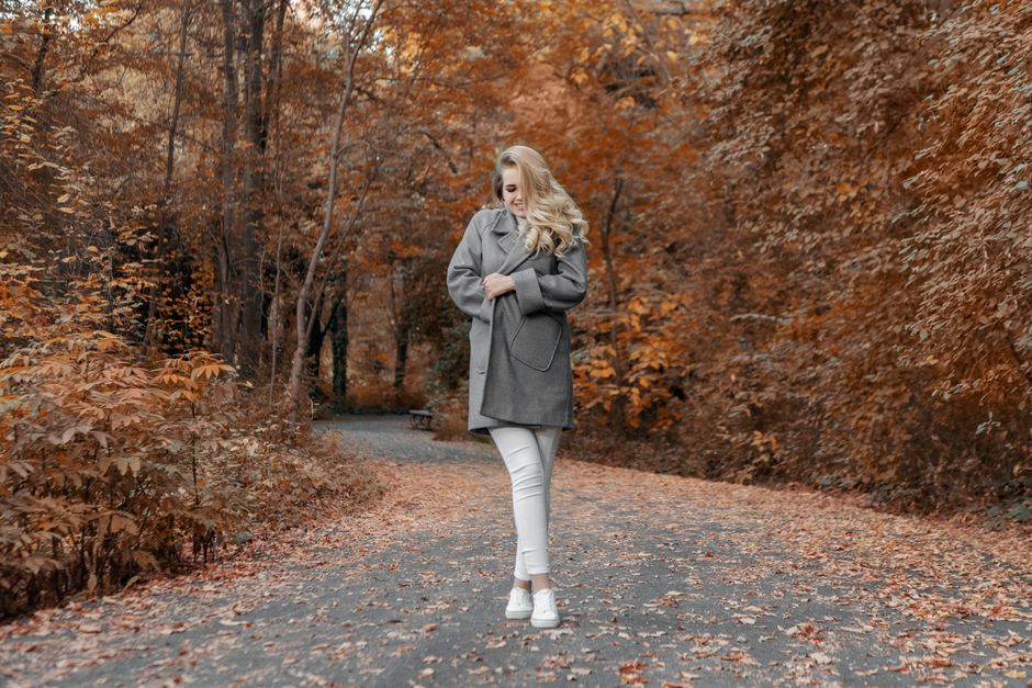 Full body happy young female bundling up in warm cozy coat while standing on asphalt road
