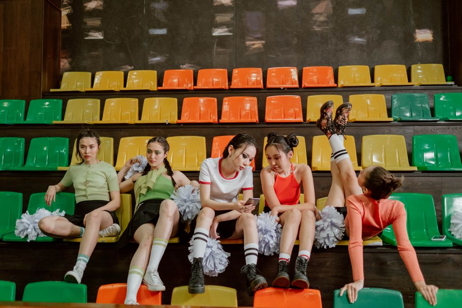 A group of young cheerleaders sitting and relaxing on colorful stadium seats indoors.