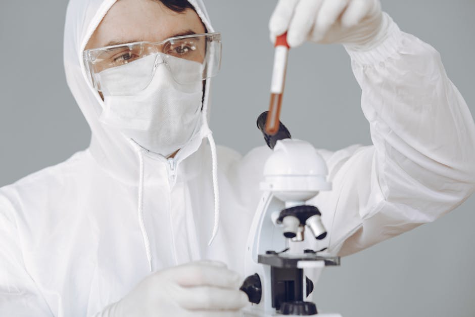 A scientist in protective gear examines a blood sample using a microscope in a lab.