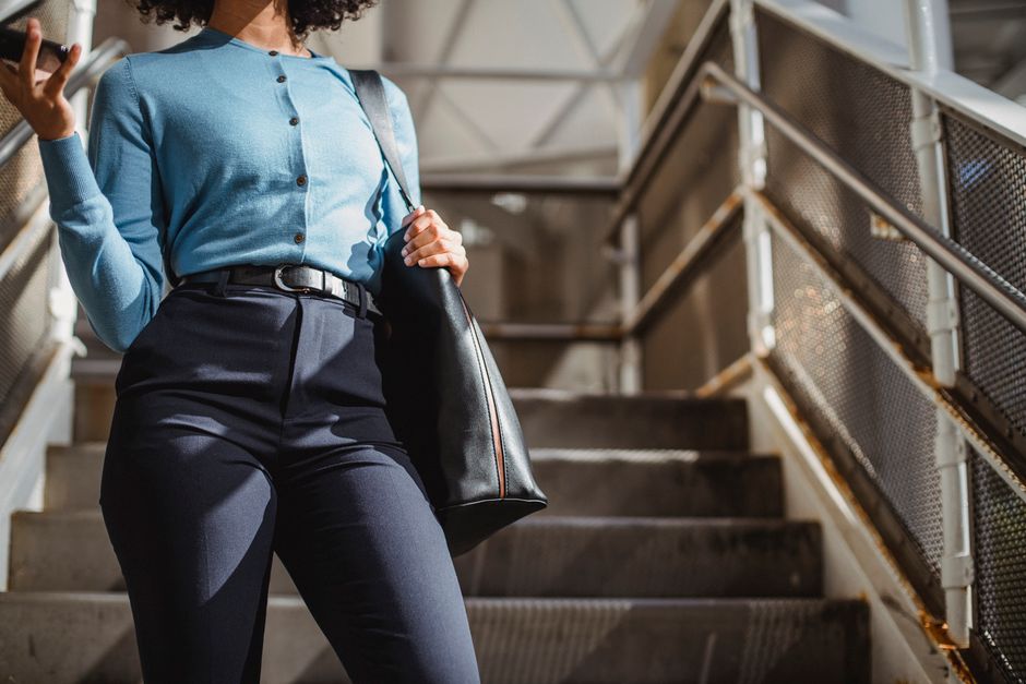 From below of unrecognizable African American female with bag standing on staircase near railing while browsing cellphone on sunny street