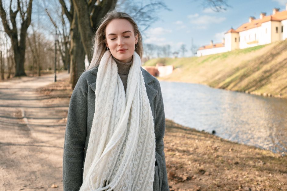 Portrait of a woman in a cozy scarf and coat by a riverside path during winter.