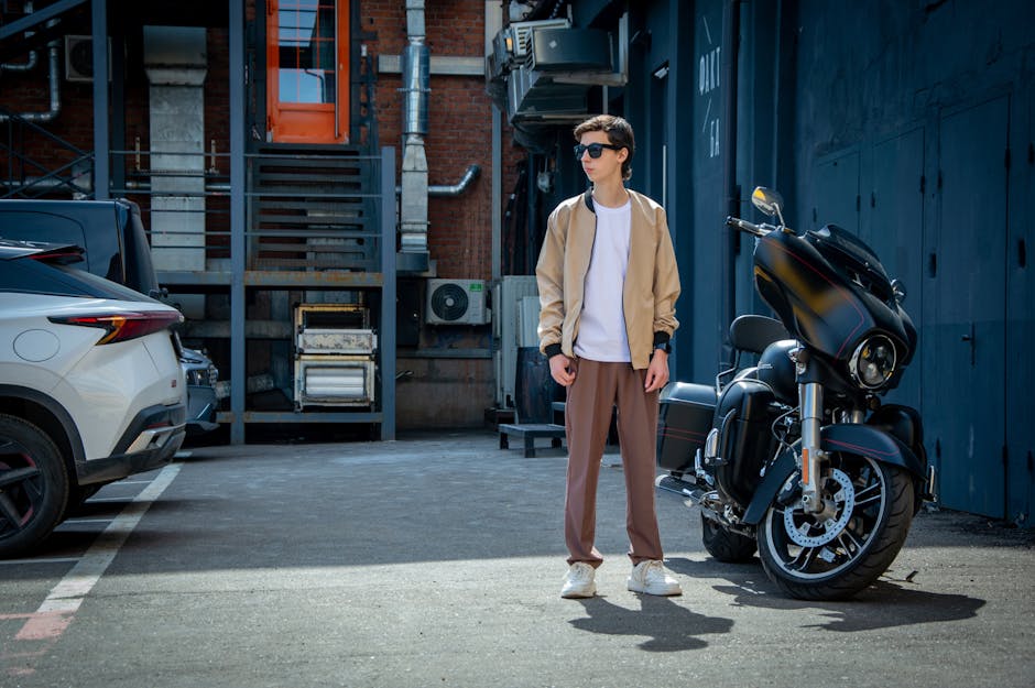 Young man in urban alley with motorcycle and modern outfit.
