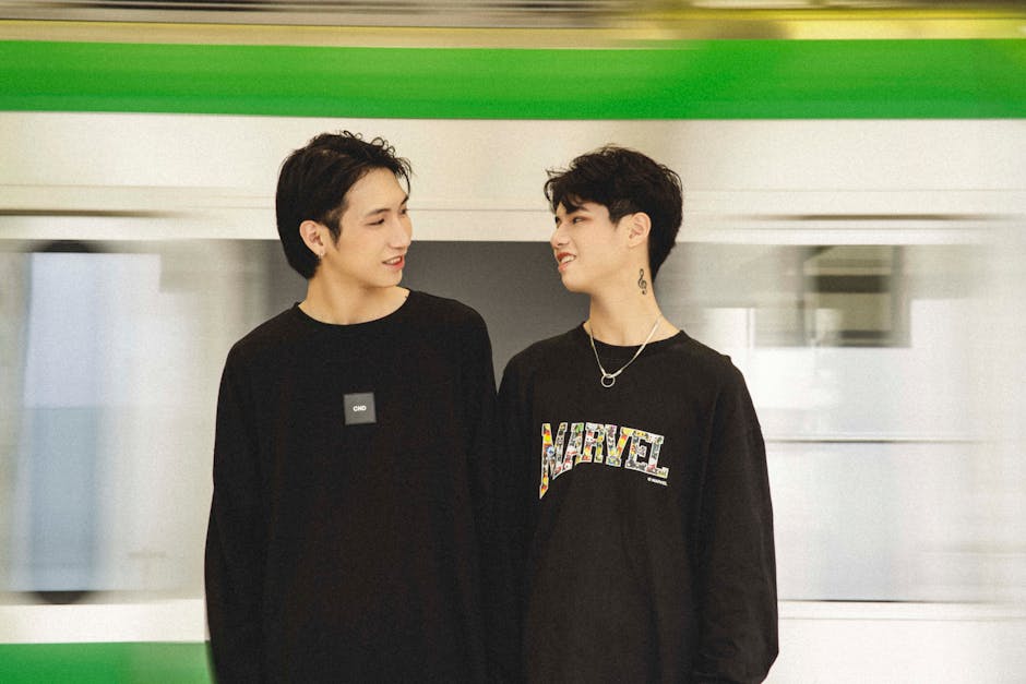 Two Asian men in black pullovers at an urban train station, embodying modern fashion and urban lifestyle.