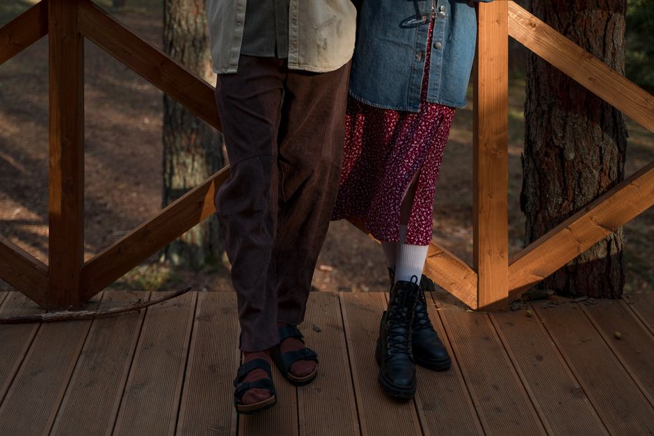 Legs of a couple standing on a rustic wooden deck amidst a serene forest setting.