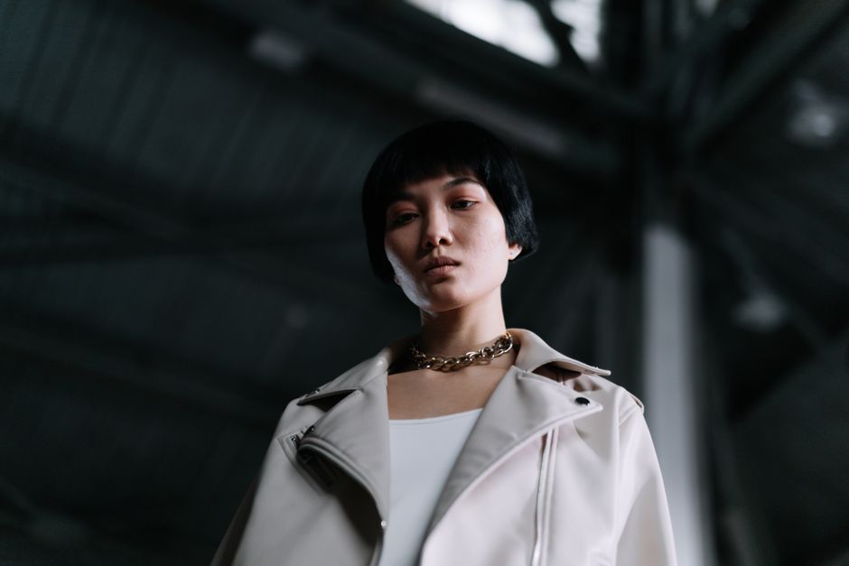 Low angle portrait of a woman with black hair and chain necklace, exuding confidence in an