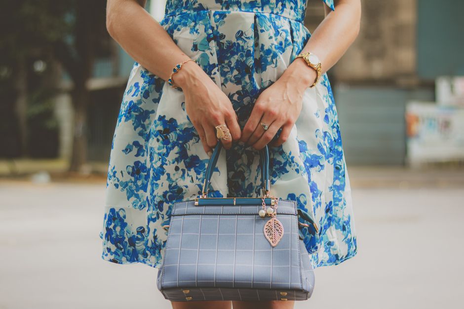 Elegant woman in blue floral summer dress holding a chic handbag outdoors.