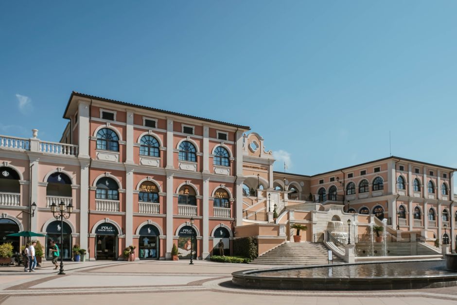 Beautiful Italianate shopping piazza featuring a fountain and classic architecture under a clear blue sky.