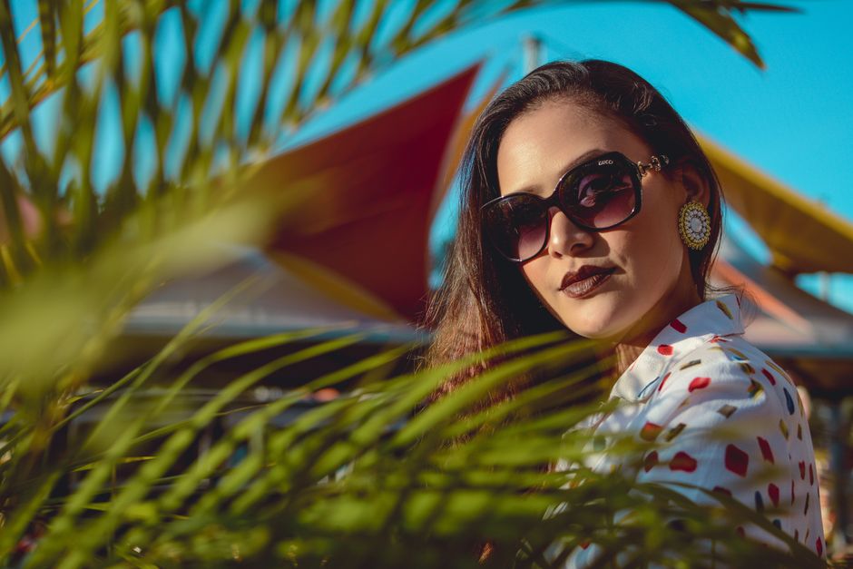 Fashionable woman wearing sunglasses and patterned blouse in a vibrant outdoor setting.
