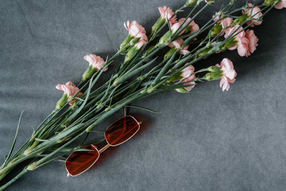 A stylish arrangement of pink flowers and sunglasses on a grey background.