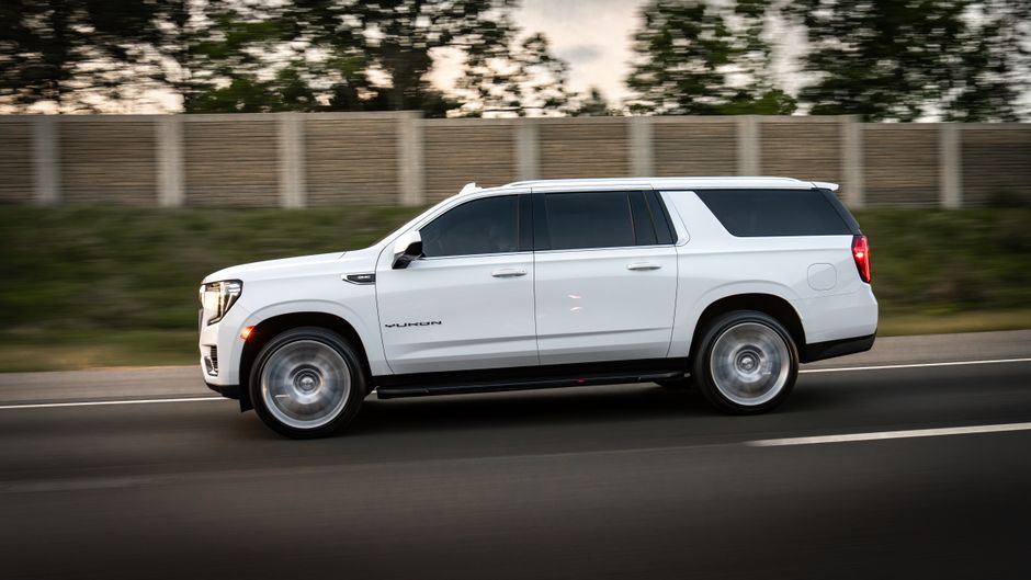 A white GMC Yukon XL drives quickly down a highway, showcasing its sleek design and powerful presence.