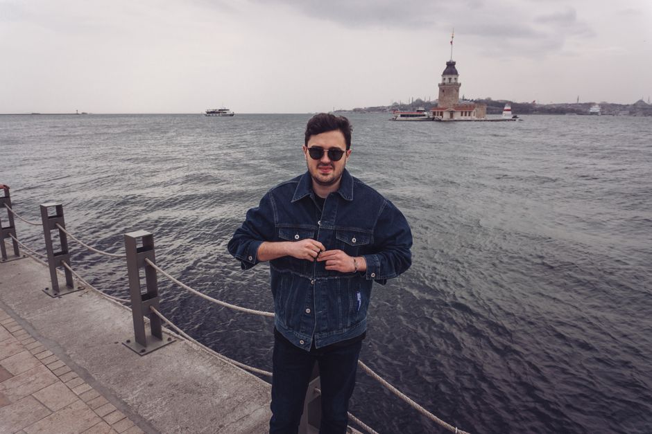 Casually dressed man stands by the sea, Maiden's Tower visible in Istanbul, creating a relaxed vibe.