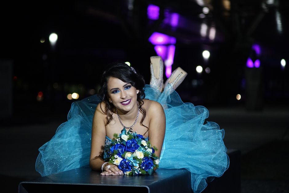 A woman in a sparkling blue gown poses with a vibrant floral bouquet at nighttime, exuding elegance.