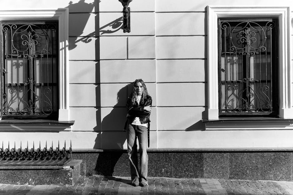 Black and white photo of a person leaning against a building wall, conveying a moody urban vibe.