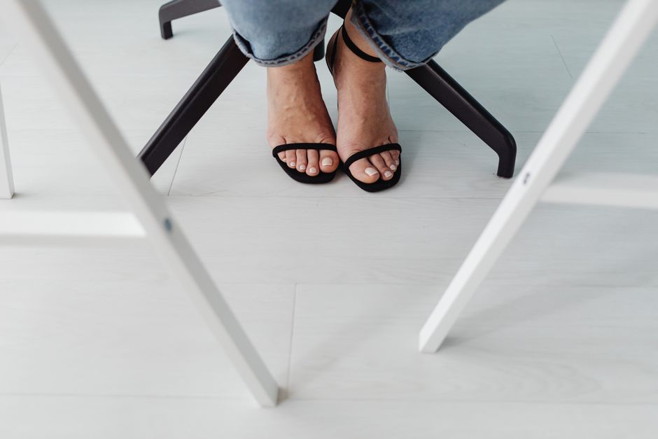 Person wearing stylish black sandals under a table, showcasing a casual and modern look.