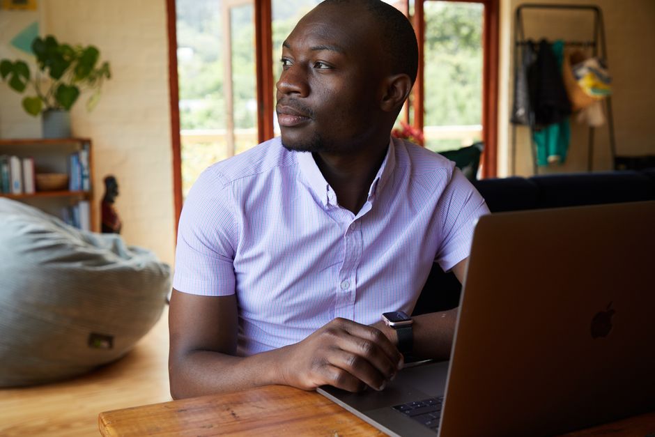 Serious African American male freelancer in formal wear sitting at wooden table while brow