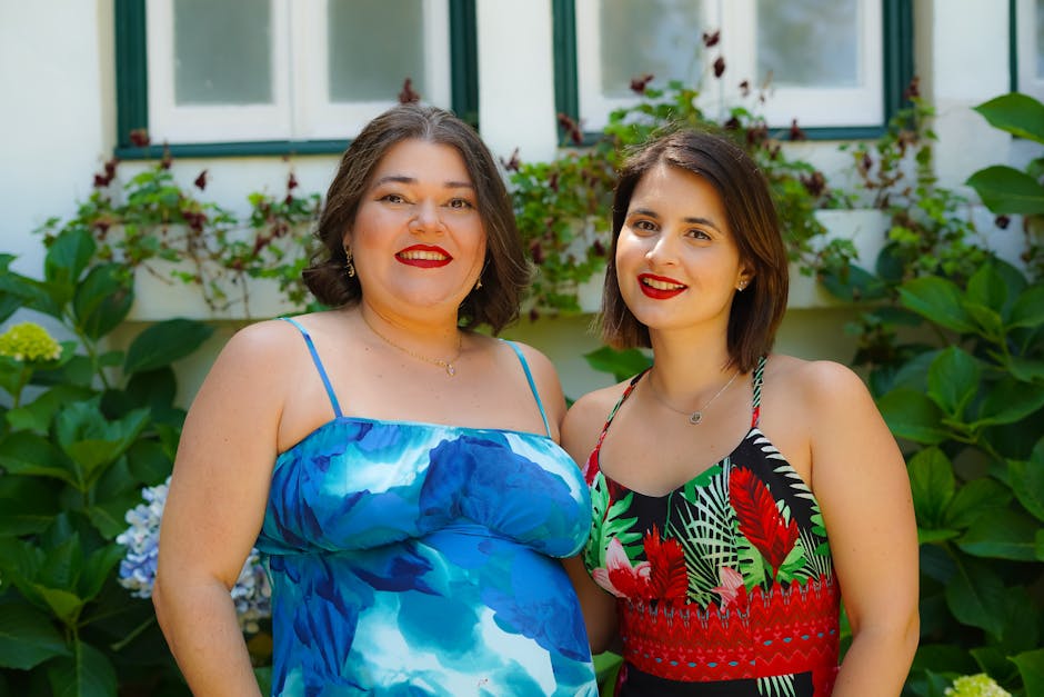 Two women with bright smiles pose in colorful summer dresses against a floral backdrop in Sintra, Portugal.