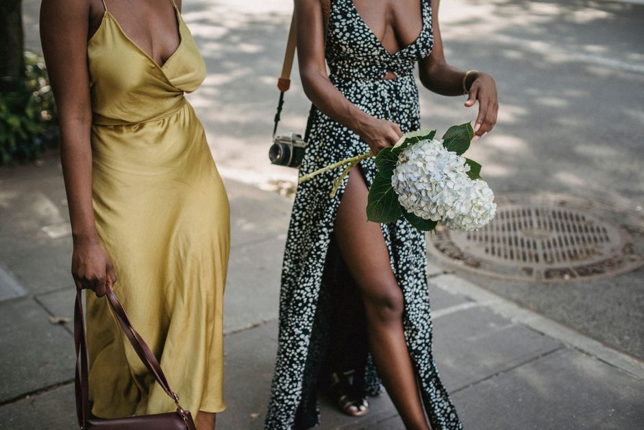 Two stylish women on a sidewalk holding white hydrangeas, embodying fashion and elegance.