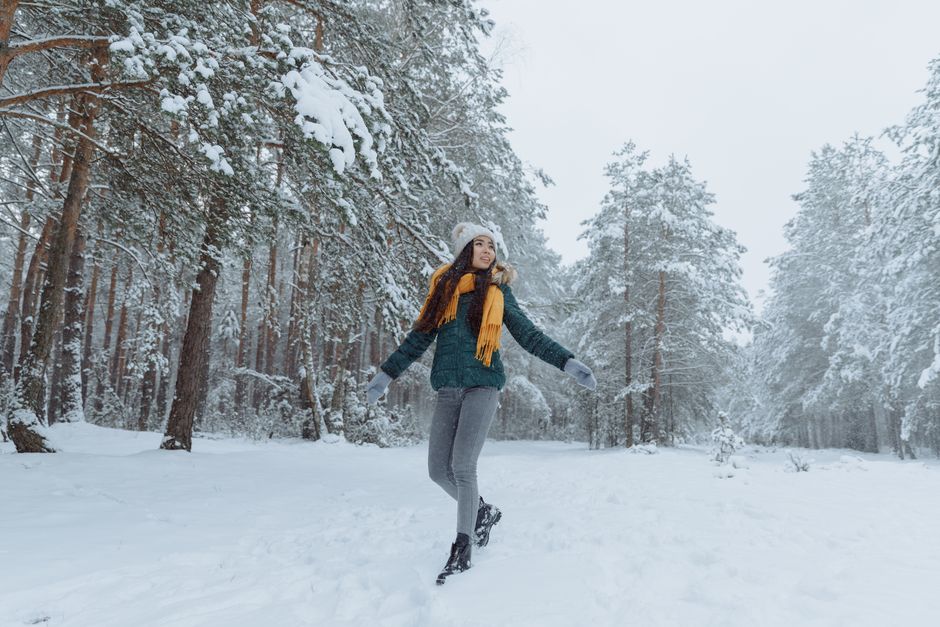 A woman smiles while walking in a snowy forest, embracing the winter season.