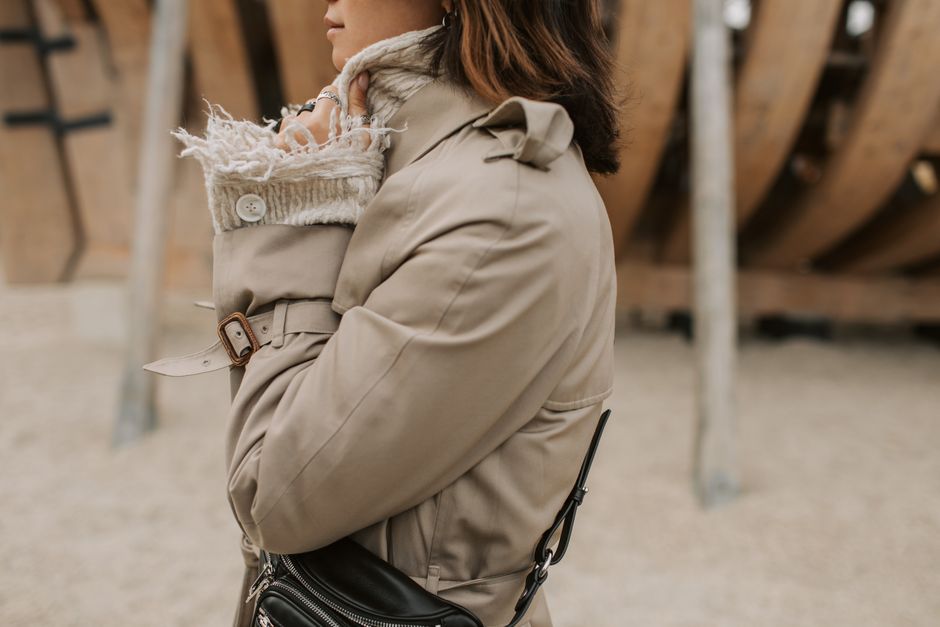 Fashionable woman in a beige coat, side view, outdoors with a sling bag.